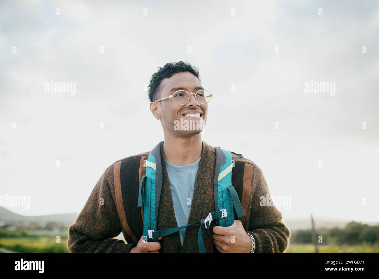 Jeune homme souriant avec sac à dos randonnée sous le ciel Banque D'Images