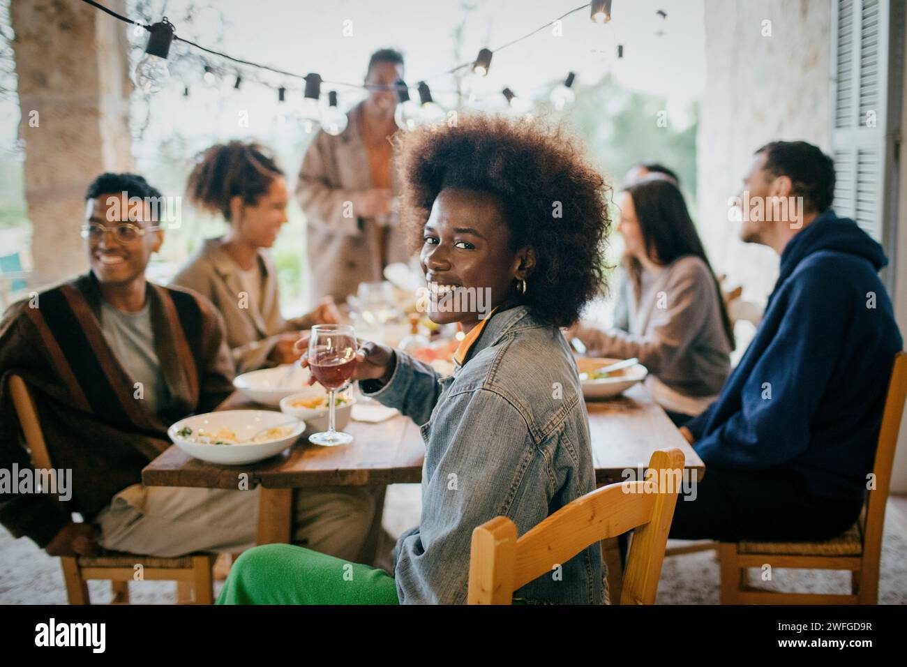 Portrait de femme heureuse avec coiffure afro tenant le verre à vin pendant le dîner dans le patio Banque D'Images