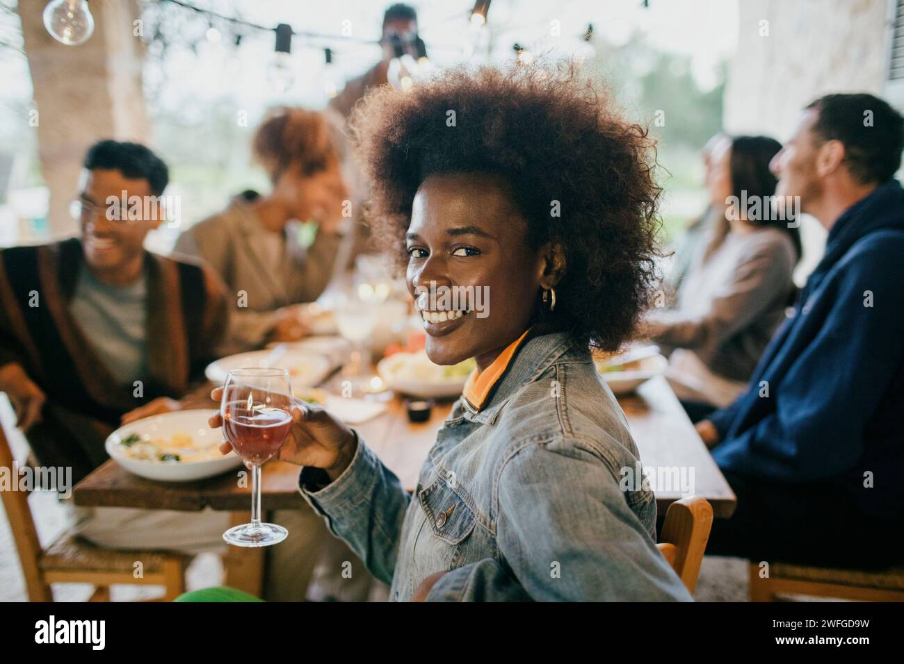 Portrait souriant de jeune femme avec coiffure afro tenant le verre à vin Banque D'Images