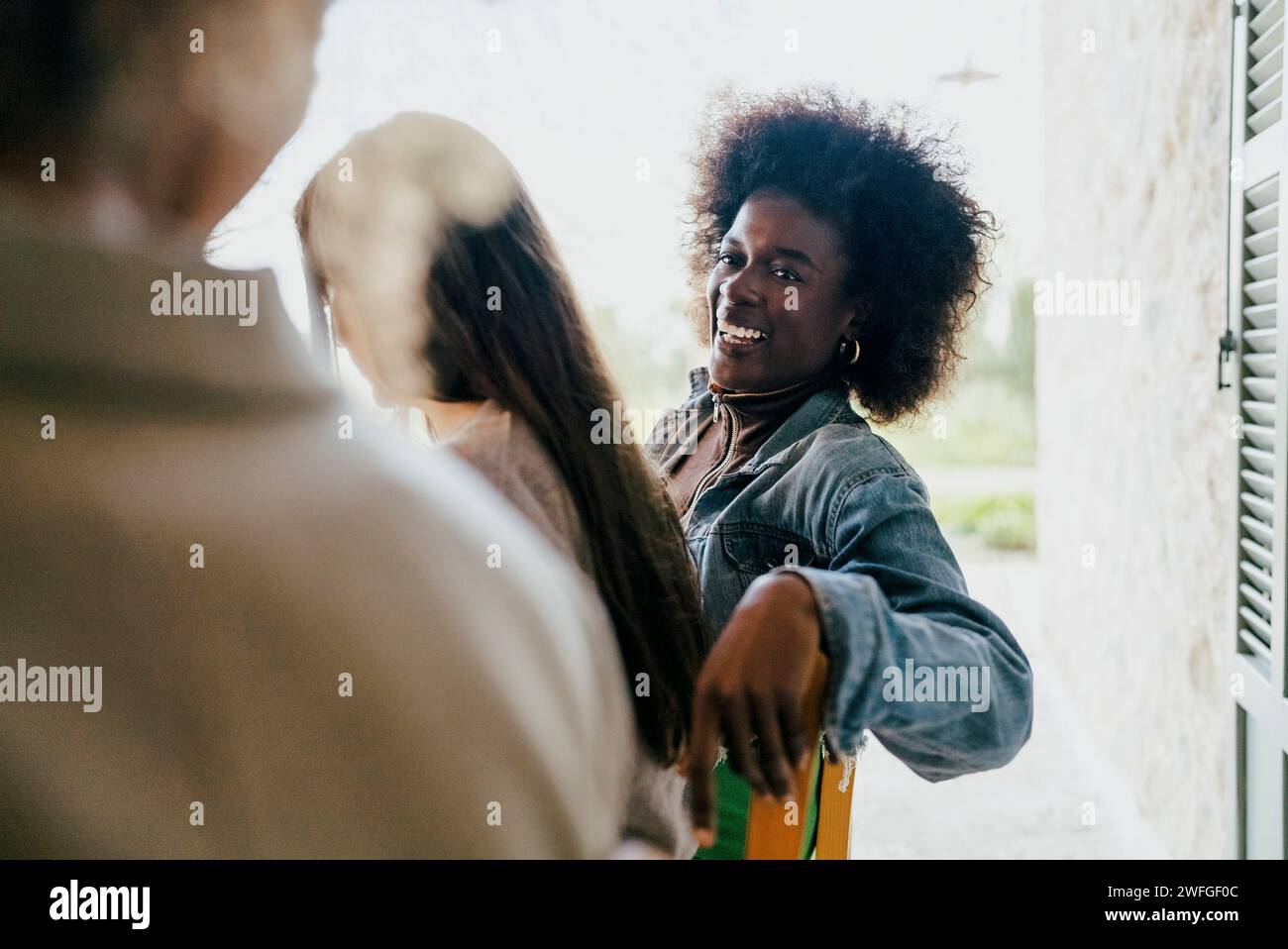 Femme heureuse avec coiffure afro assis par des amis féminins dans le patio Banque D'Images