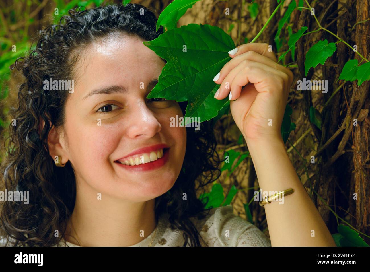 Portrait vertical de la jeune Latina vénézuélienne avec des bigoudis, heureux debout posant souriant regardant la caméra avec la feuille de plante grimpante sur le mur, la vie est Banque D'Images