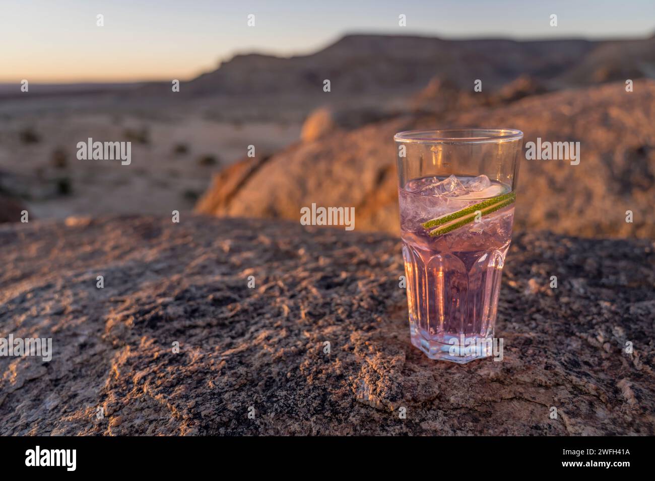 Verre avec gin tonic rose sur rocher de dolérite dans le désert, tourné dans la lumière brillante du coucher du soleil de la fin du printemps près de Hobas, Namibie, Afrique Banque D'Images