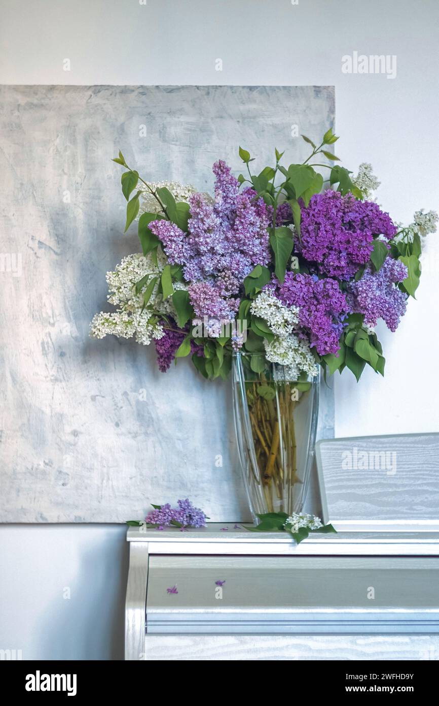 un bouquet de lilas dans un vase transparent sur un fond texturé clair. image verticale de fleurs lilas, violettes et blanches. carte printemps ou été. flou de mise au point Banque D'Images