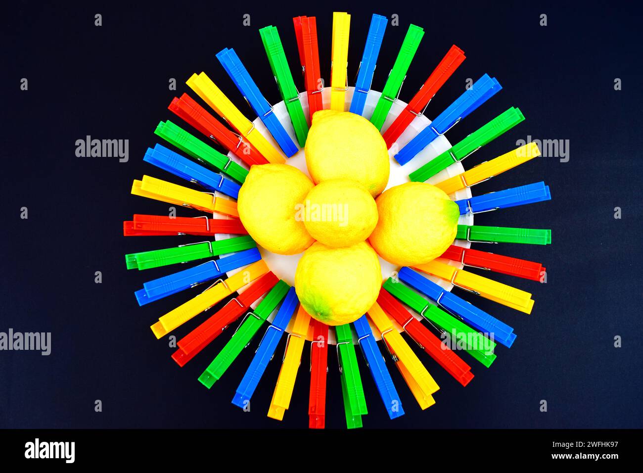Un cercle rond,fait de pinces à linge en plastique coloré et un tas de citrons frais assis au milieu. Banque D'Images