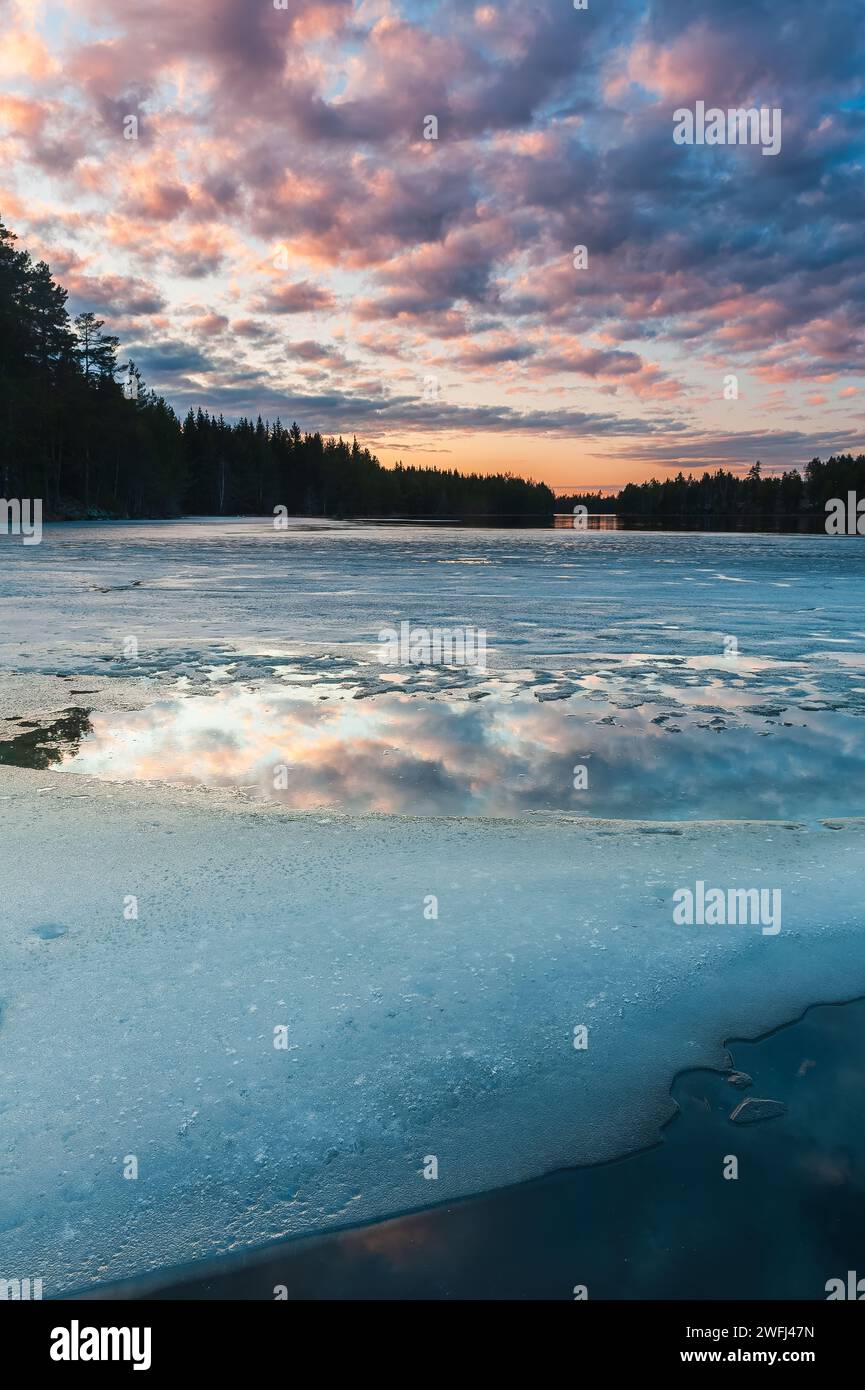 Une scène tranquille capture la beauté d'un lac partiellement gelé au crépuscule, avec des teintes subtiles du coucher de soleil se reflétant sur la glace et l'eau au milieu des s. Banque D'Images