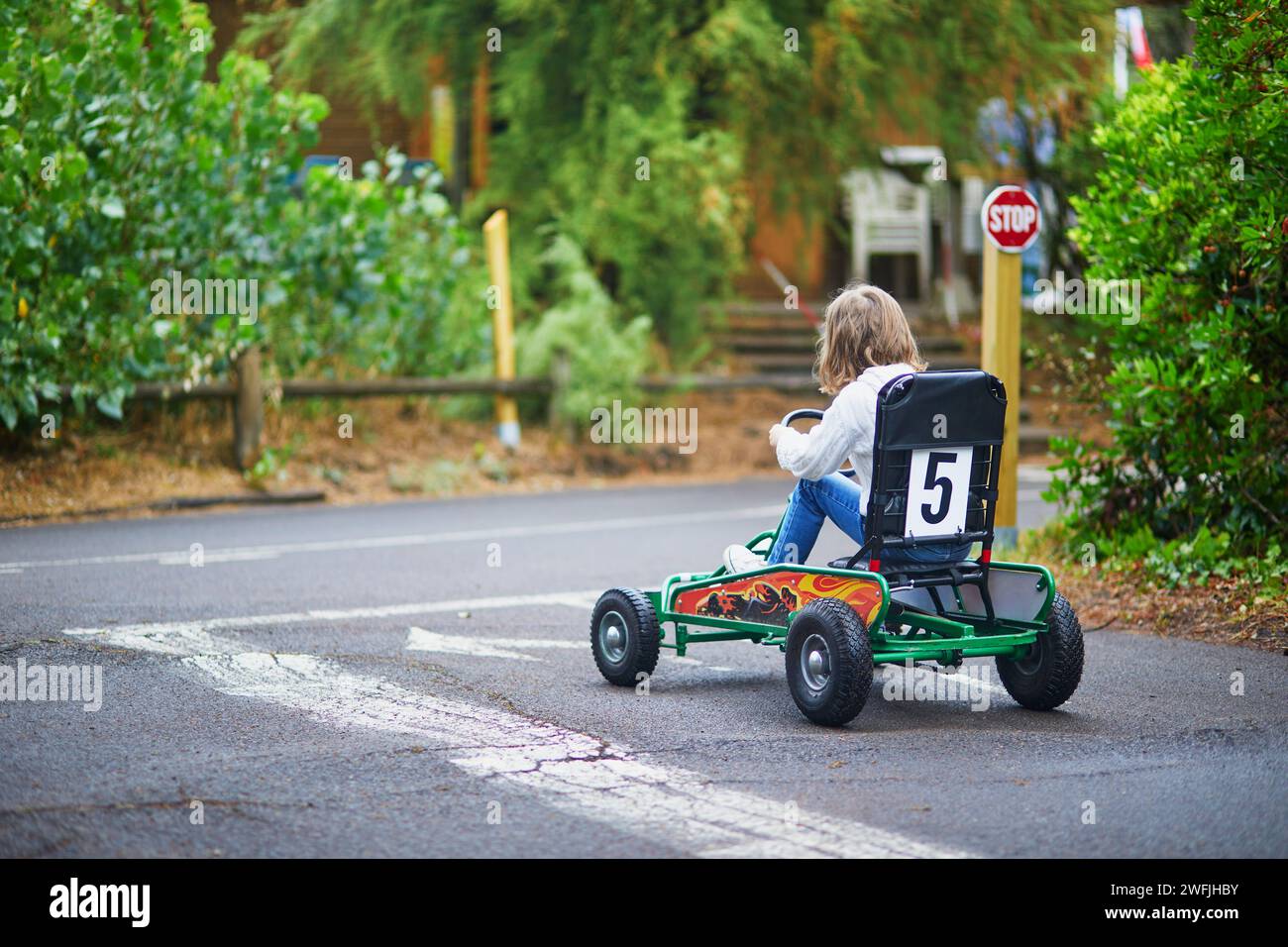 Fille d'enfant d'âge préscolaire conduisant la voiture de course à pédale dans le parc d'attractions avec marquage de surface de route et feux de circulation Banque D'Images