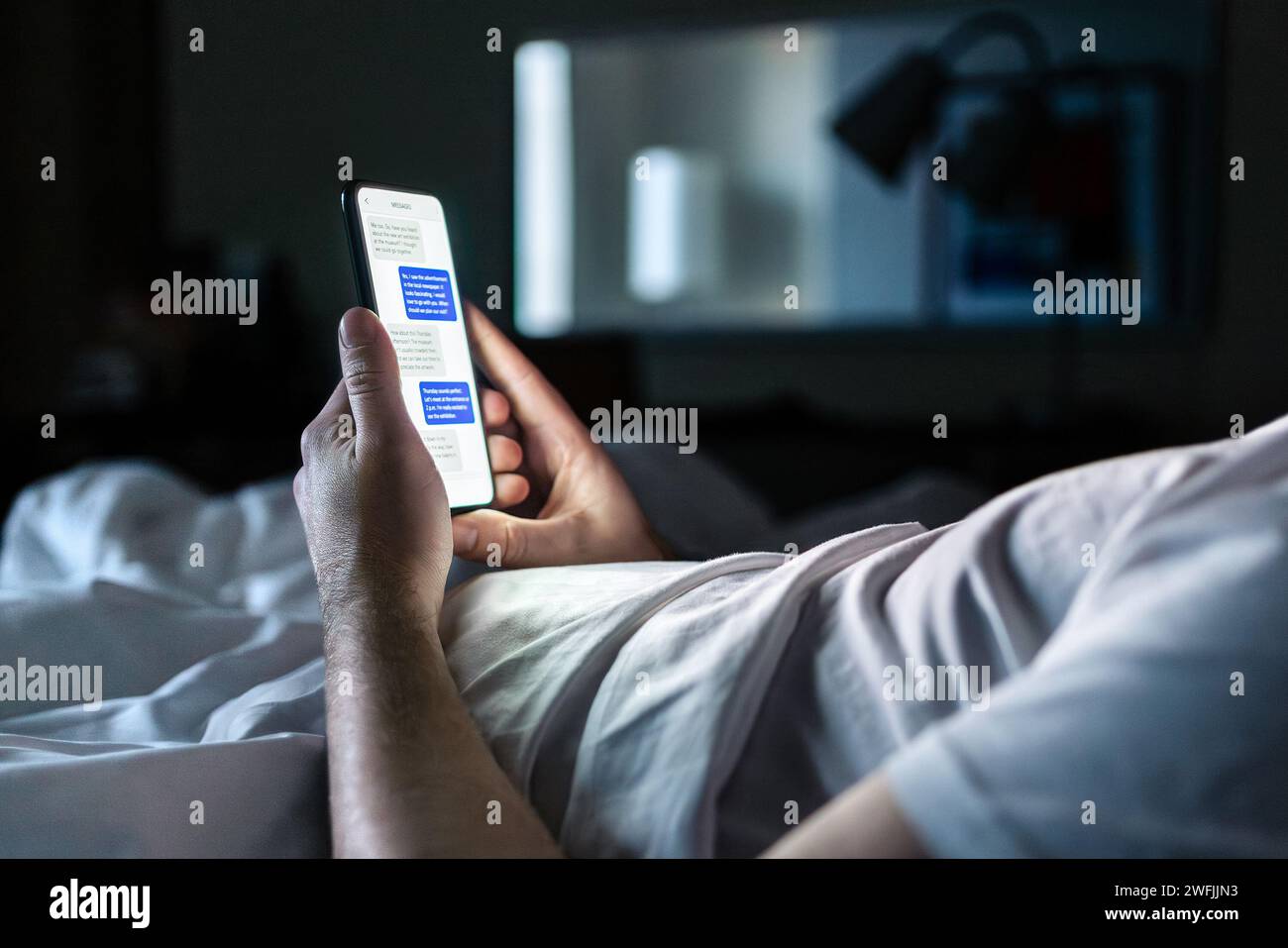 Téléphone dans le lit. Chat par SMS sur l'écran du smartphone la nuit. Homme dans la chambre à coucher sombre de la maison ou la chambre d'hôtel. Rencontres en ligne, escroquerie mobile sms ou secret. Banque D'Images
