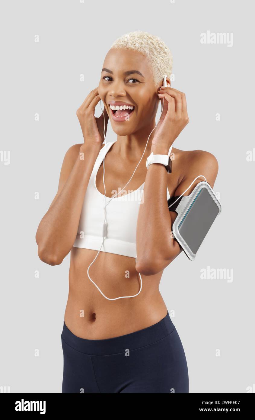 Séance d'entraînement de fitness, femme souriante heureuse porte des écouteurs de téléphone portable sur le bracelet, athlète féminine africaine latino-américaine en vêtements de sport, l'exercice en g Banque D'Images