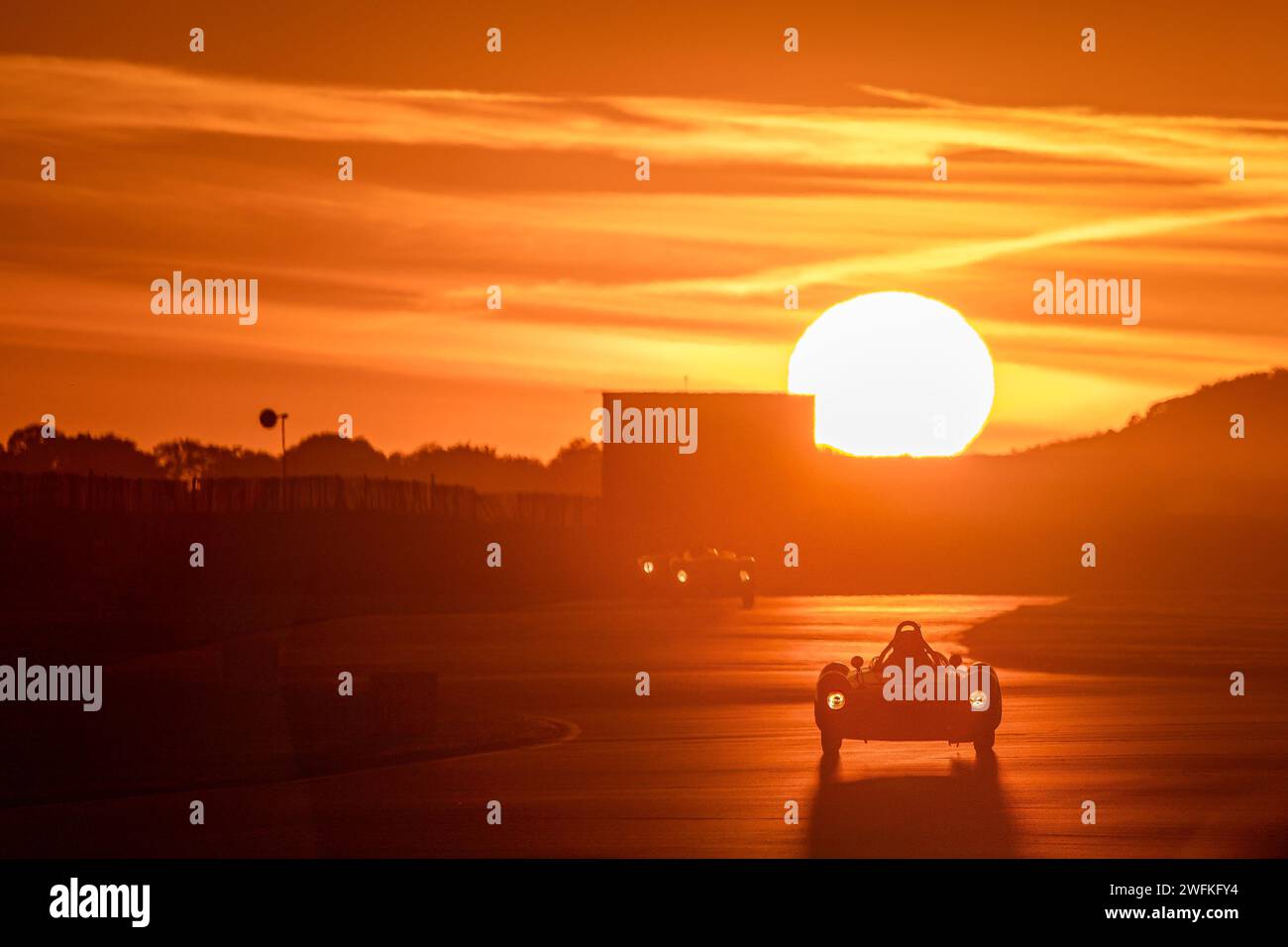 Le soleil couchant sur le circuit automobile de Goodwood met en lumière un participant à la course nocturne du trophée commémoratif Freddie March Banque D'Images