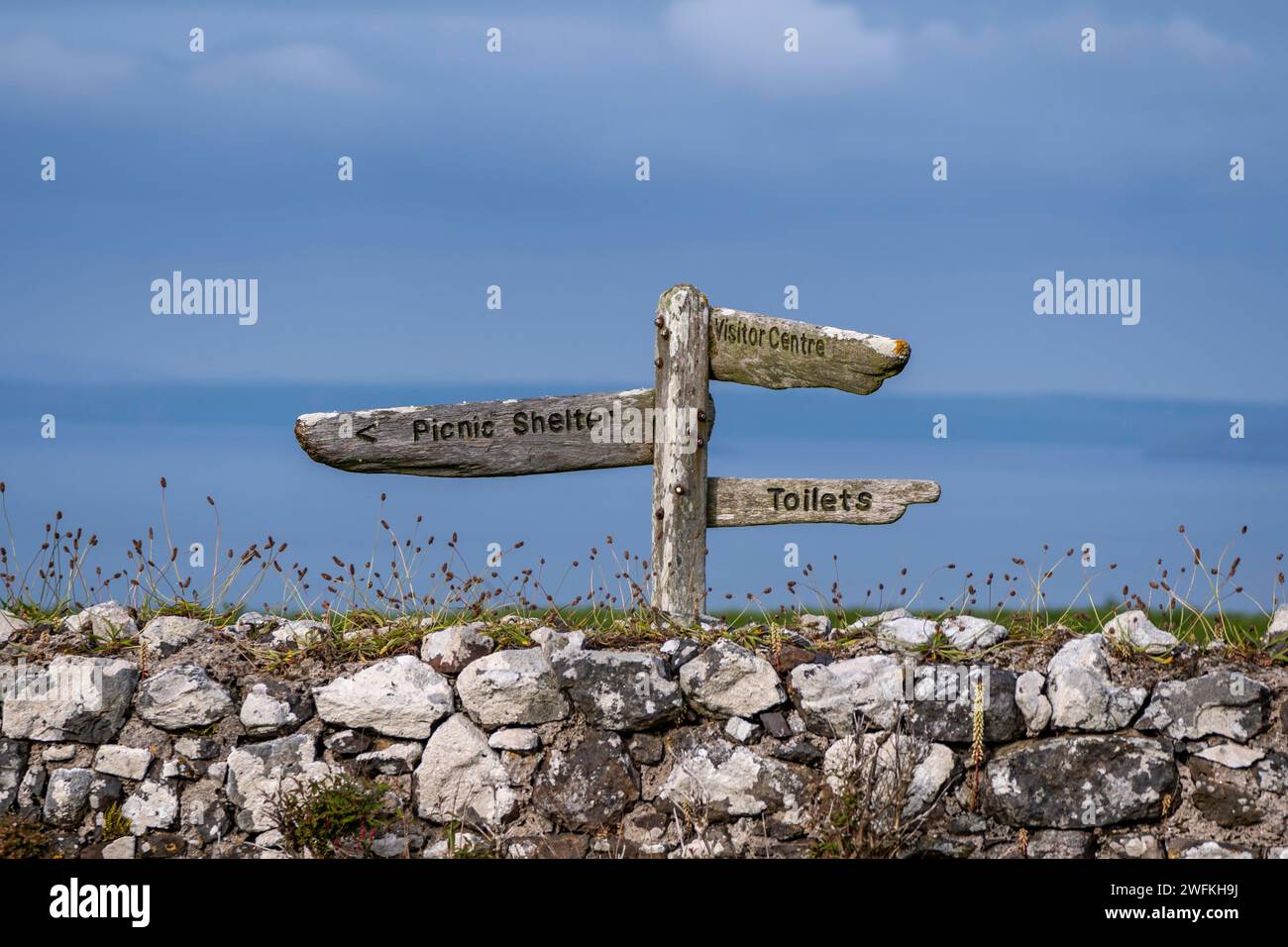 Un vieux poteau de signalisation en bois worldy le long du mur de briques sur l'île de Skomer au large de la côte du Pembrokeshire au pays de Galles un jour d'été. Banque D'Images