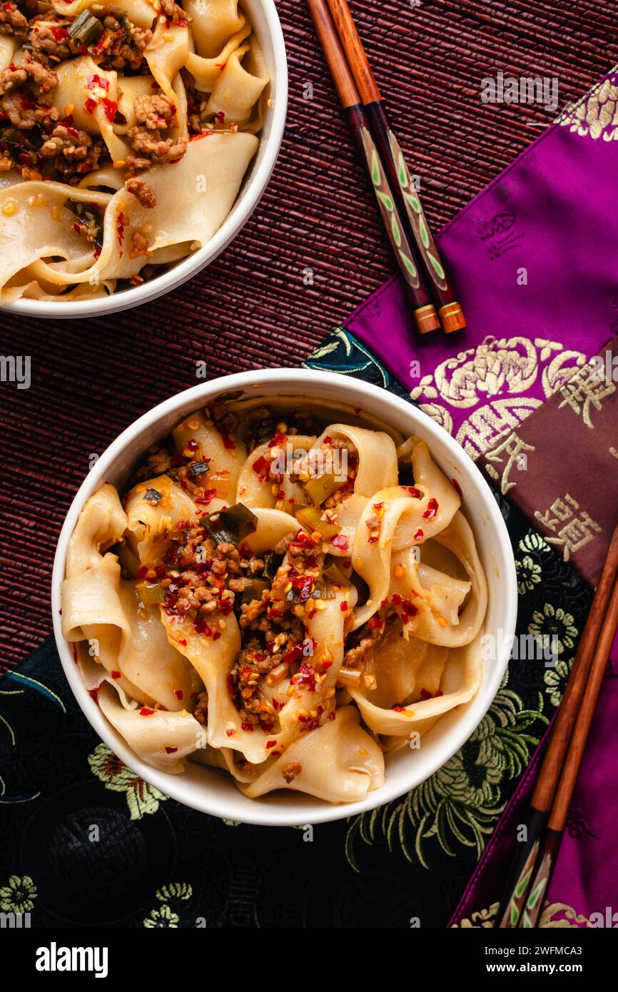 Bols de nouilles Biang Biang garnis de sauce épicée à l'huile de Chili : Biang Biang mian garni de porc haché et d'huile de Chili servi dans des bols avec des baguettes Banque D'Images