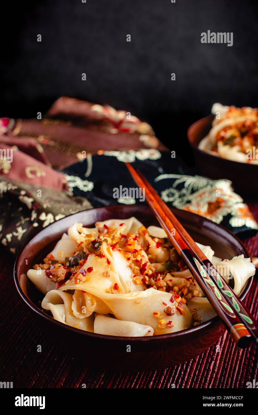 Nouilles Biang Biang garnies de sauce épicée à l'huile de Chili gros plan : Biang biang mian garni de porc haché et d'huile de Chili servi dans des bols avec des baguettes Banque D'Images