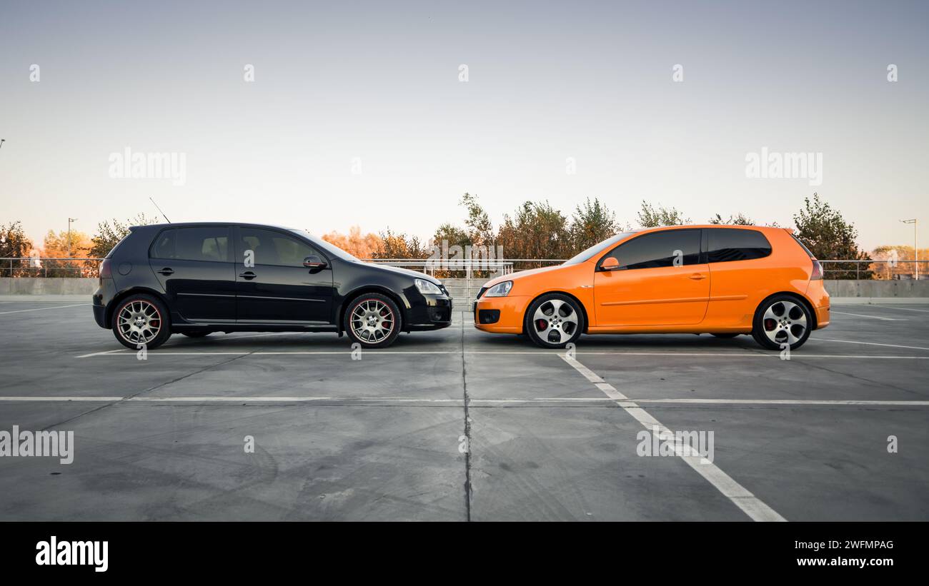 Côté de Golf GTi noir et orange garé sur un grand parking vide. Vue latérale de deux Volkswagen à hayon Banque D'Images