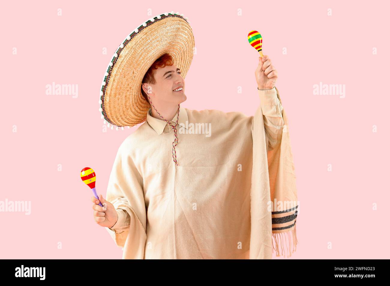 Portrait de jeune homme mexicain en sombrero, poncho et maracas sur fond rose Banque D'Images