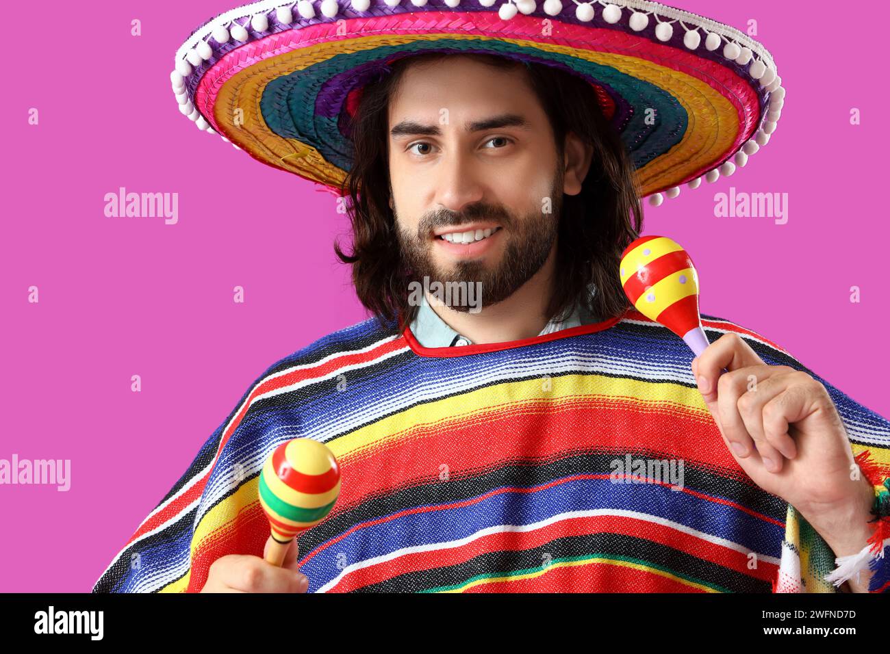 Beau jeune homme mexicain en sombrero, poncho et avec des maracas sur fond magenta Banque D'Images