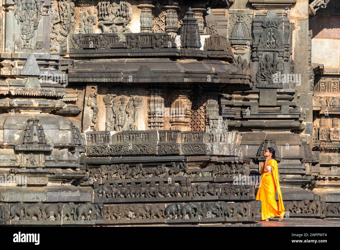 Belur, Karnataka, Inde - janvier 9 2023 : une femme indienne portant un saree orange vif appréciant les sculptures antiques au temple de Chennakeshava. Banque D'Images