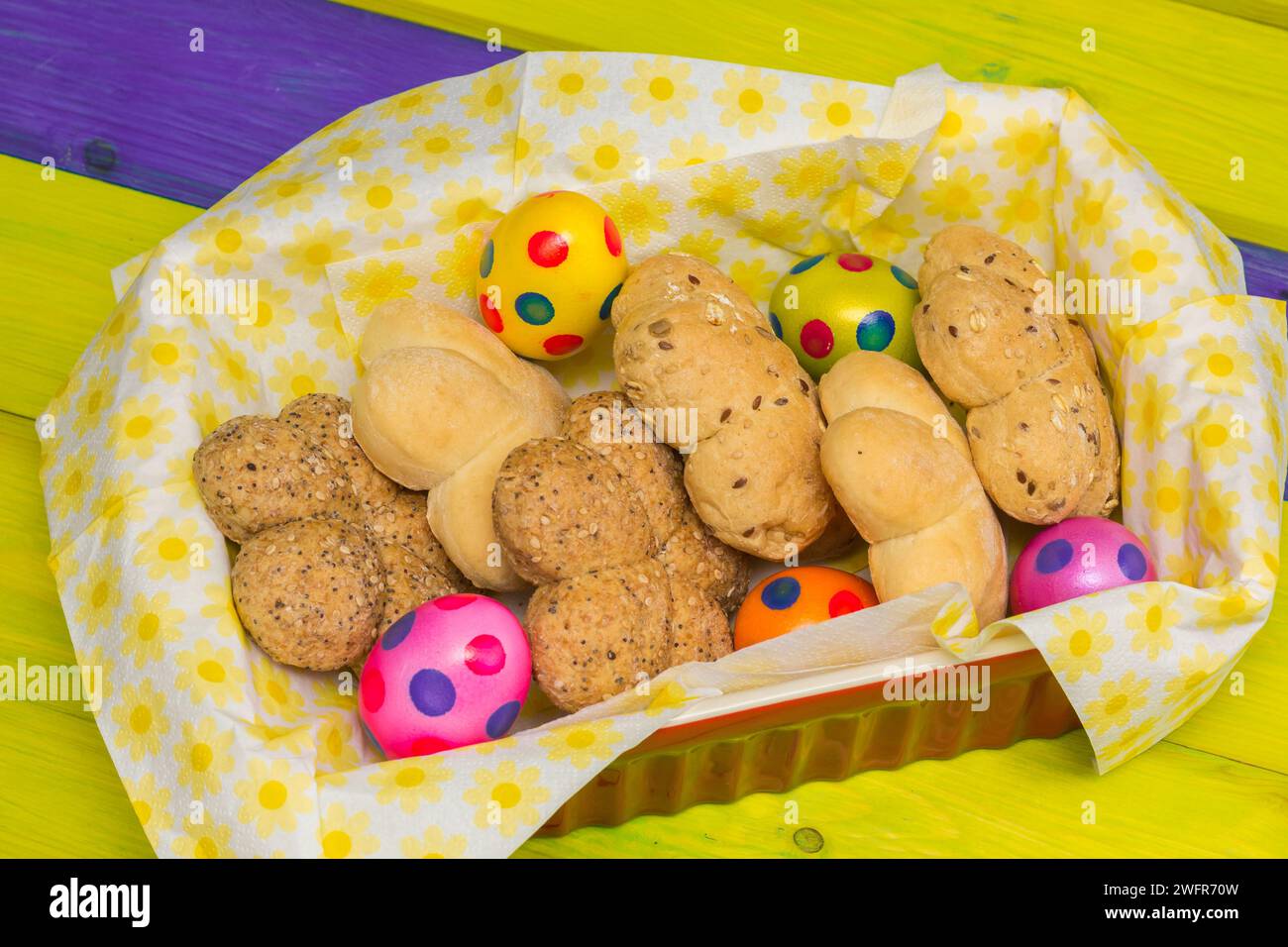 Petits pains et œufs de pâques colorés dans un panier sur une table en bois jaune Banque D'Images