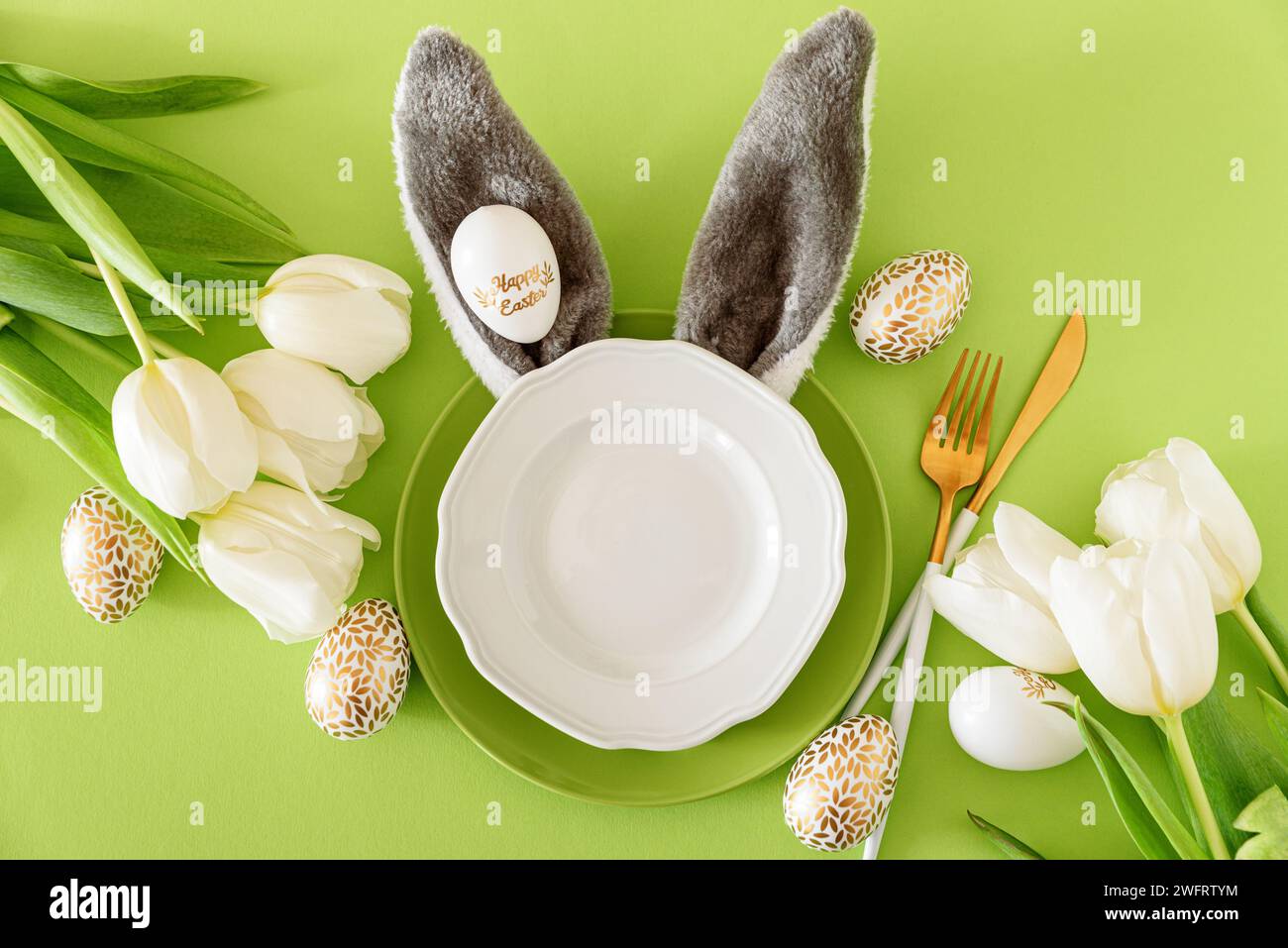 Assiette vide décorée oreilles de lapin, tulipes blanches et oeufs de Pâques sur fond vert. Concept de célébration de Pâques. Pose à plat. Vue de dessus Banque D'Images