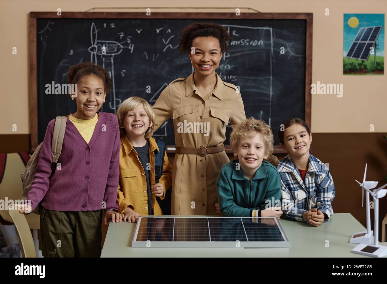 Portrait de la jeune femme noire comme enseignante avec divers groupes de petits enfants debout contre le tableau noir en classe tout souriant à la caméra Banque D'Images