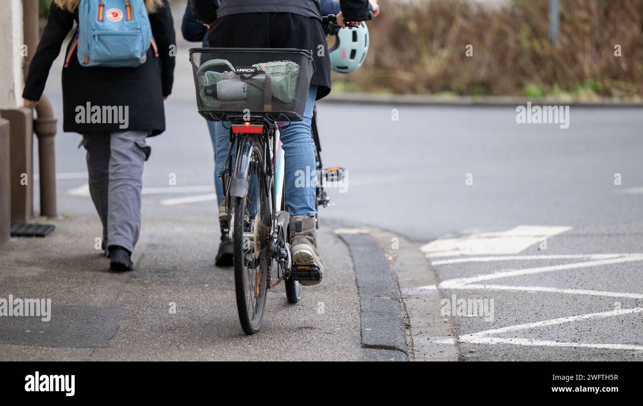 , Alltagssituation, Deutschland, 01.02.2024, Zwei Personen gehen auf einem Gehweg, eine davon schiebt ein Fahrrad mit einem Korb und einem Helm auf d Banque D'Images