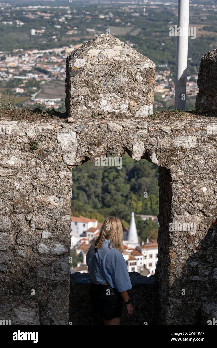 Femme regardant à travers l'embrasure du mur médiéval bataille du château des Maures au Palais national de Sintra à Sintra, Portugal. Banque D'Images
