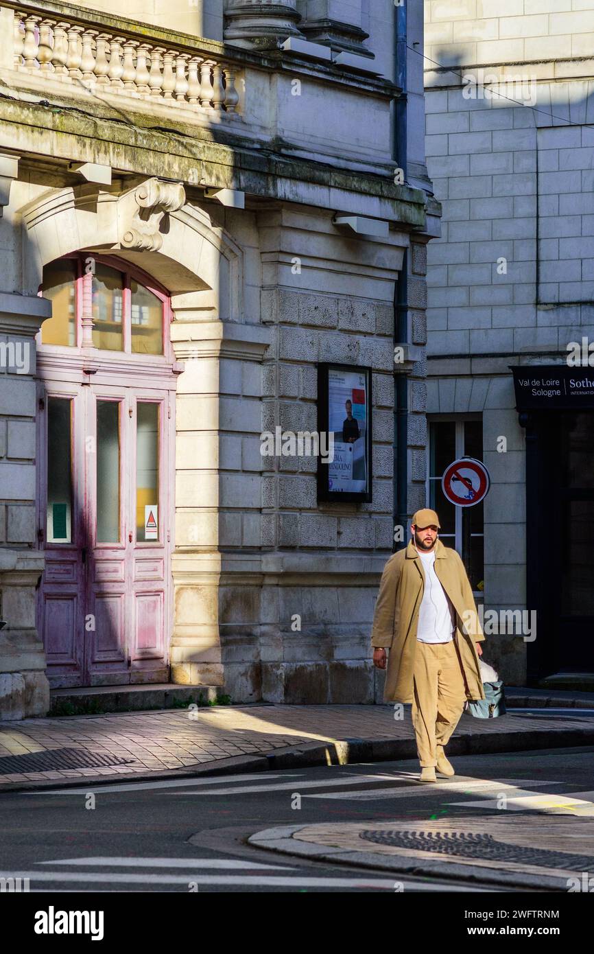 Homme bien habillé marchant à travers le puits de lumière du soleil dans le centre-ville - Tours, Indre-et-Loire (37), France. Banque D'Images