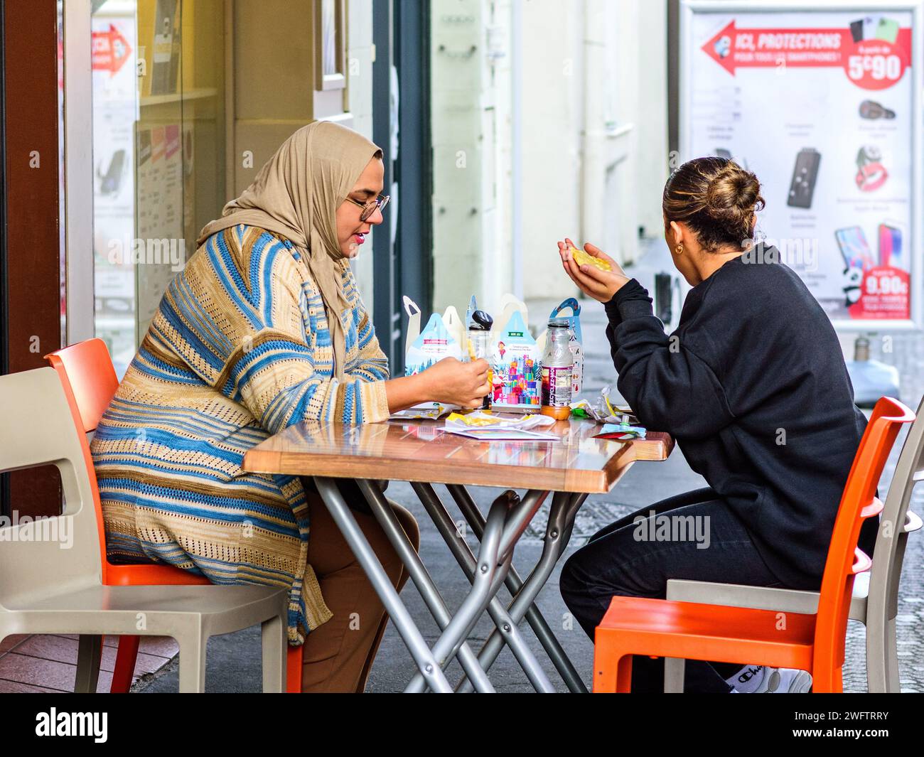 Deux femmes (une arabe) mangeant à table de café en plein air - Tours, Indre-et-Loire (37), France. Banque D'Images