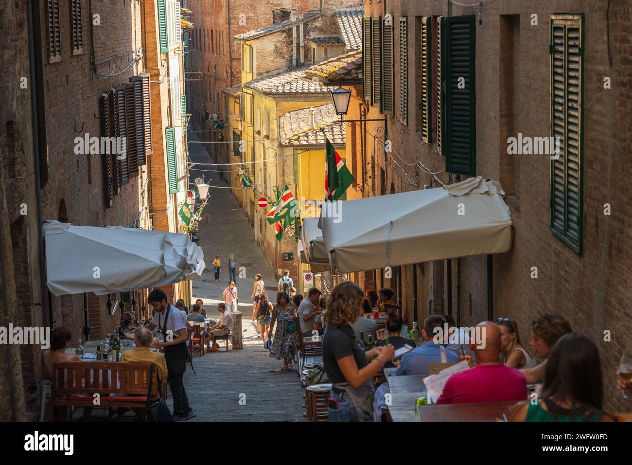 Sienne, Italie — 8 septembre 2023. Les clients dînent dans des restaurants extérieurs situés dans une rue en pente abrupte Banque D'Images