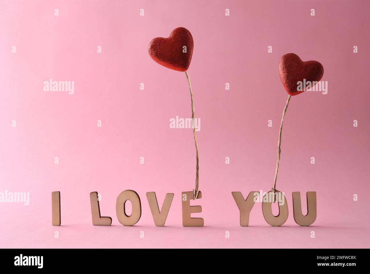 Fond d'amour avec des découpes de lettres formant la phrase je t'aime et deux ballons scintillants rouges en forme de coeur tenus par un fil de jute volant. Avant vi Banque D'Images