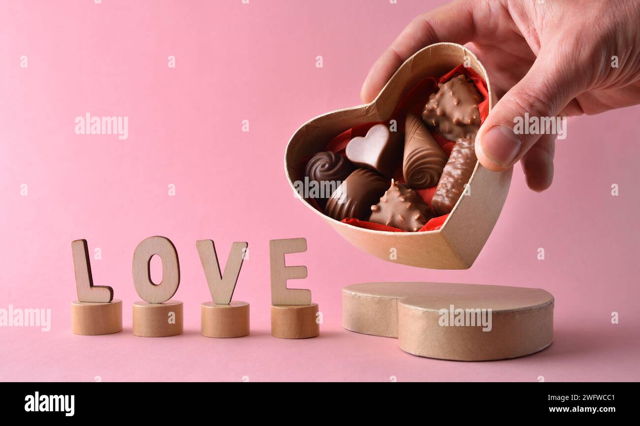 Boîte à main offrant des chocolats en forme de coeur sur fond rose avec des lettres en bois avec mot amour. Vue avant. Banque D'Images