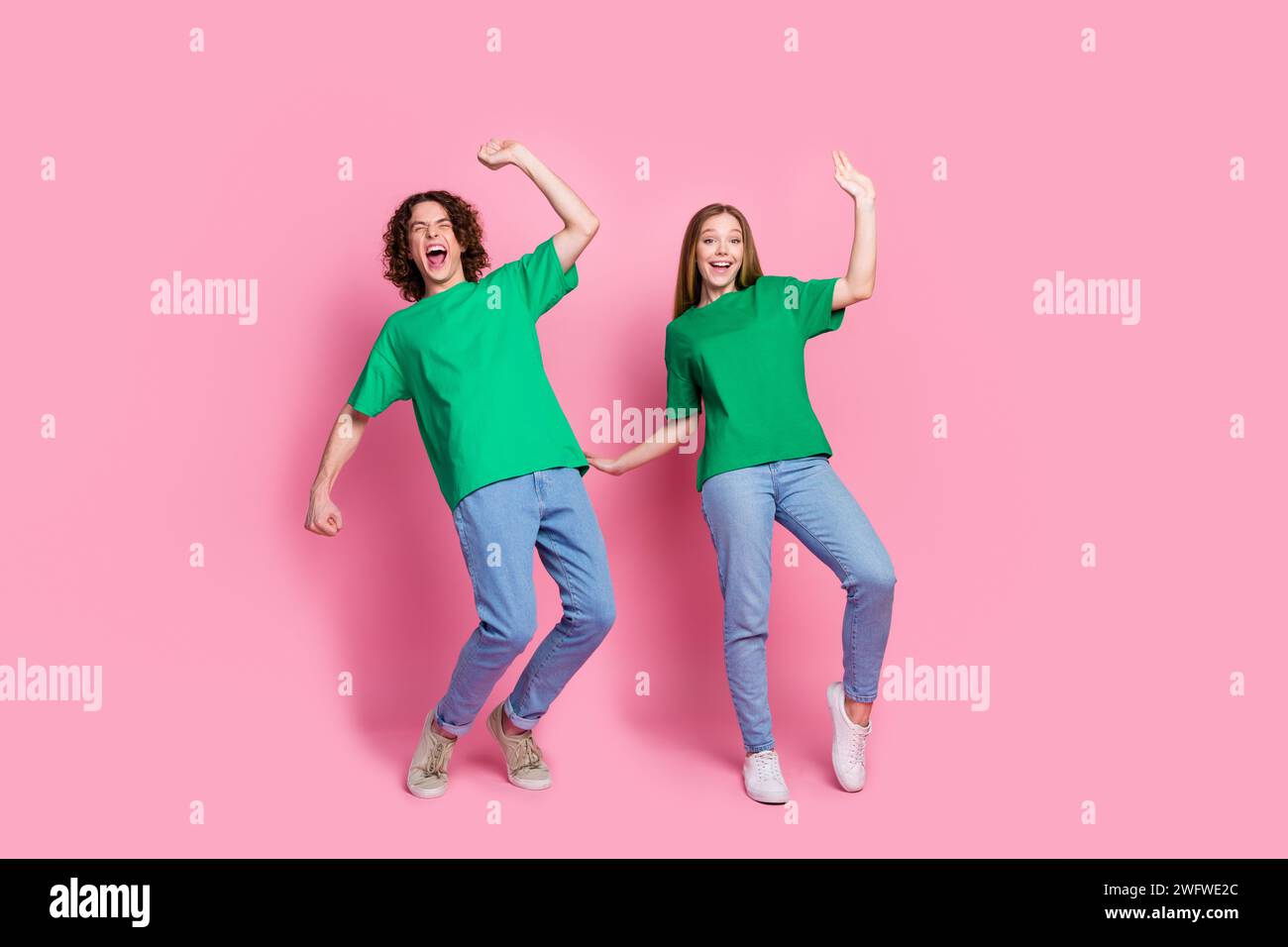 Photo pleine taille du corps de deux adolescents a une fête avec code vestimentaire t-shirt vert et jeans dansant isolé sur fond de couleur rose Banque D'Images