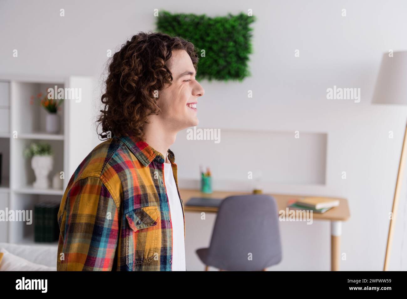 Photo de bonne humeur mec gai habillé chemise à carreaux souriant appréciant le week-end à l'intérieur de la maison chambre à la maison Banque D'Images