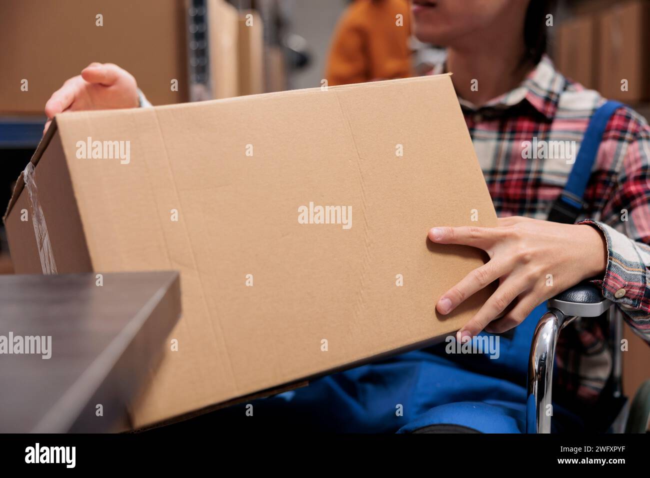 Travailleur des services postaux avec handicap tenant le paquet tout en travaillant dans l'entrepôt. Employé de magasin de société d'expédition gérant la livraison de parcles et préparant la boîte en carton Banque D'Images