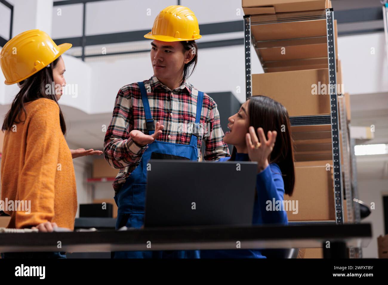 Les employés des services postaux discutent de la liste de contrôle de livraison tout en analysant les données sur ordinateur portable dans l'entrepôt. Équipe asiatique d'employés de magasin hommes et femmes discutant de la logistique des marchandises Banque D'Images