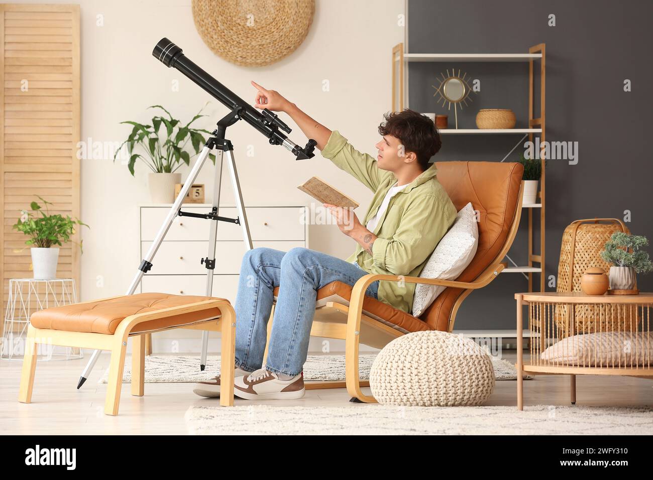 Jeune homme avec télescope et cahier assis dans un fauteuil Banque D'Images