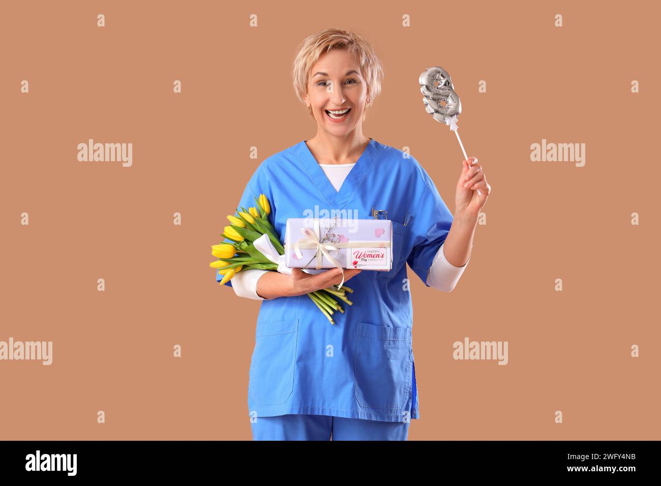 Dentiste femelle mature avec tulipes, cadeau et figure 8 sur fond brun. Célébration de la Journée internationale de la femme Banque D'Images