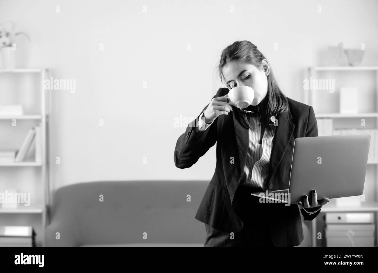 Jeune femme d'affaires sur le lieu de travail au bureau. Secrétaire femme en tenue officielle boire du café, parler au téléphone, en utilisant un ordinateur portable Banque D'Images