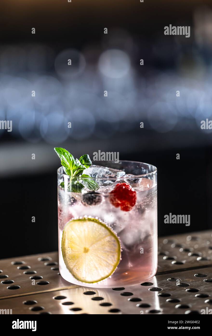 Cocktail rose Gin Tonic Drink avec framboises, myrtilles, citron vert et menthe fraîche. Banque D'Images