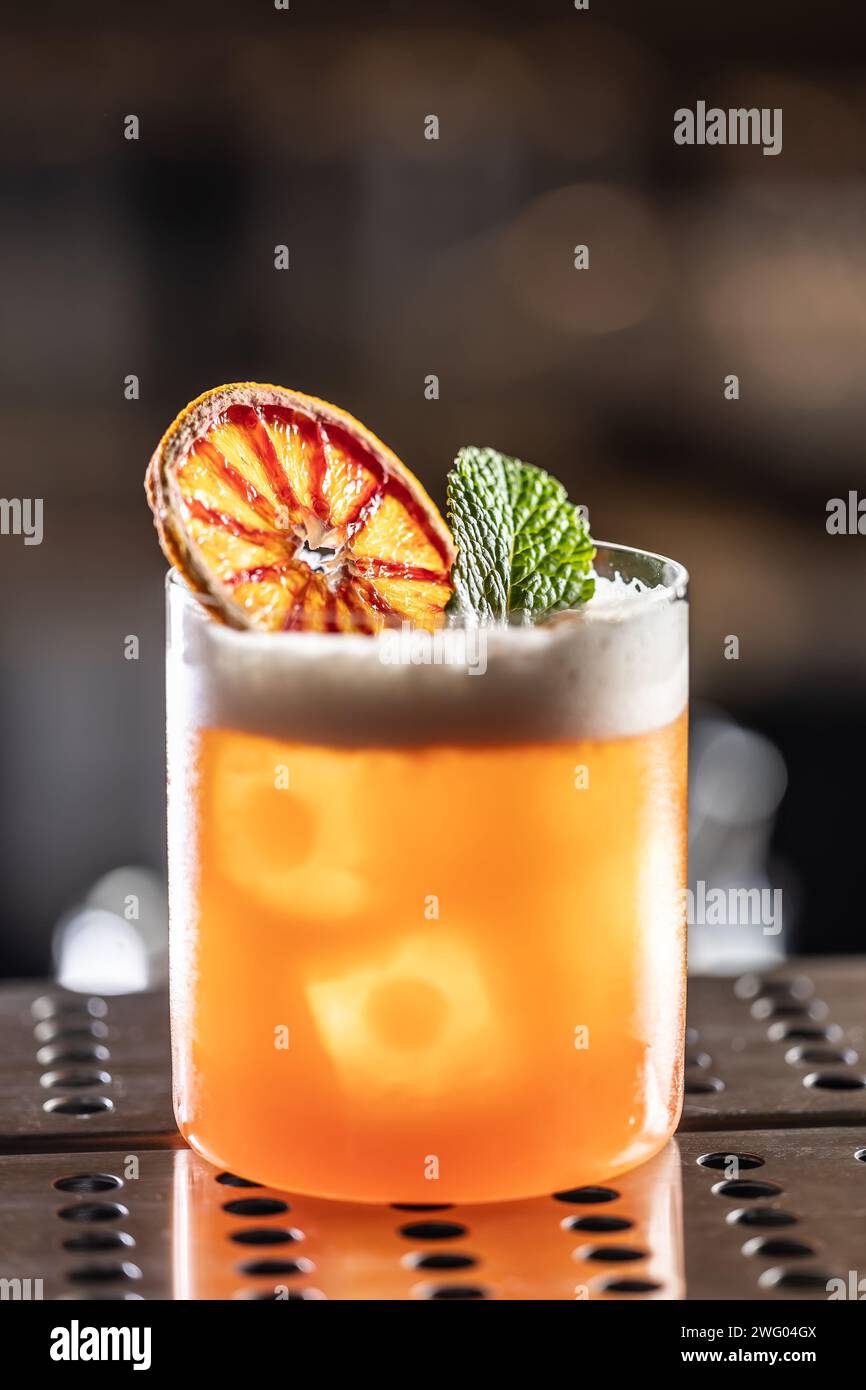 Verre de cocktail Jungle Bird garni d'orange rouge séché et de menthe sur le comptoir du bar. Banque D'Images