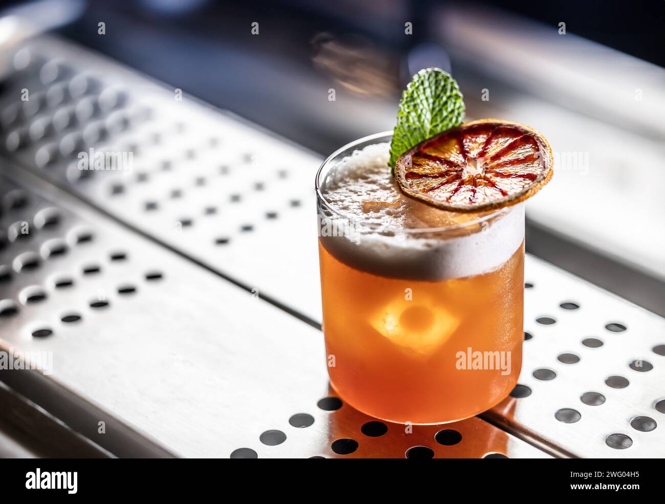 Verre de cocktail Jungle Bird garni d'orange rouge séché et de menthe sur le comptoir du bar. Banque D'Images