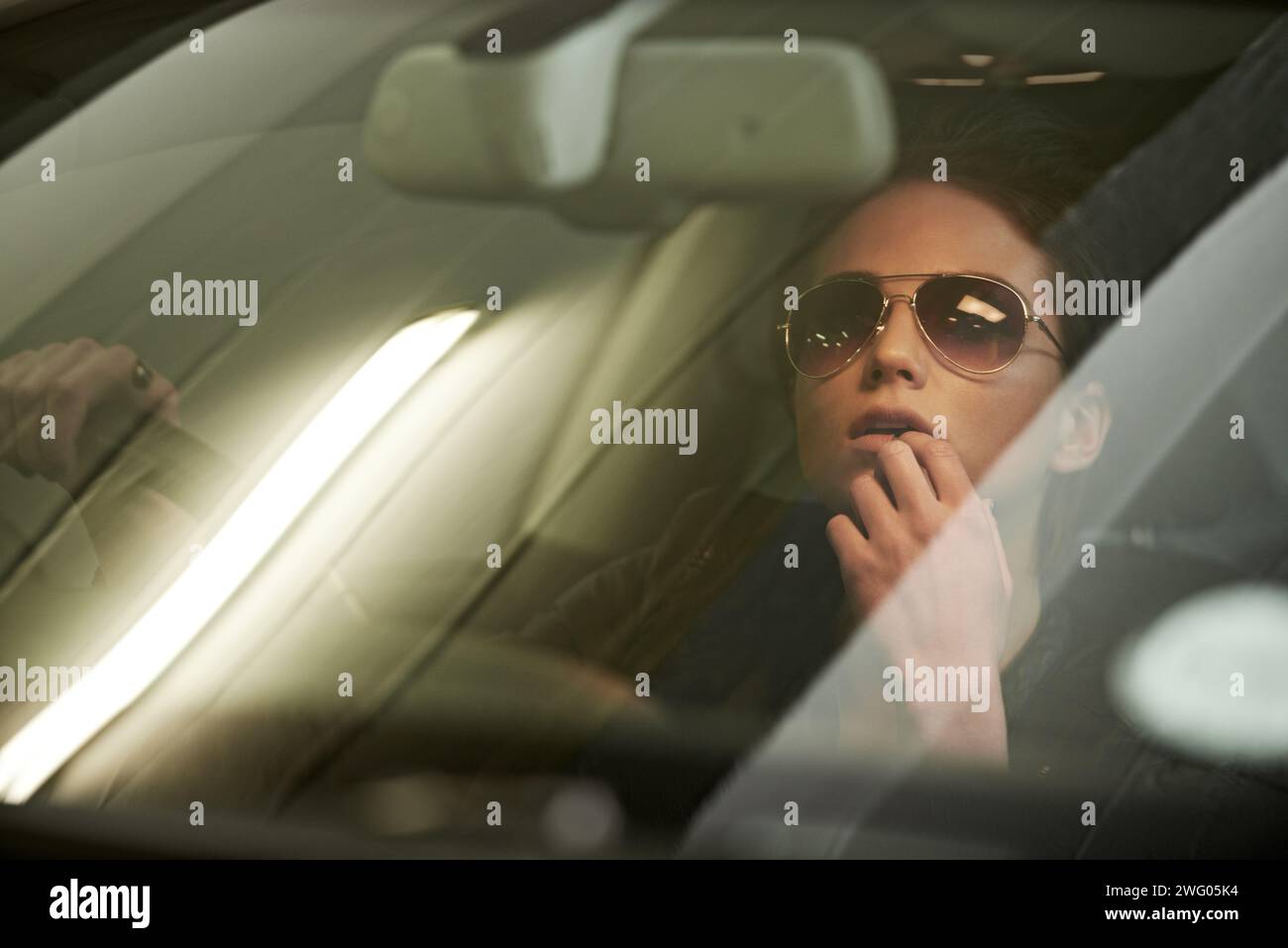 Femme, conduite et miroir à inverser du garage de stationnement pour voyage ou voyage avec des lunettes de soleil. Visage, personne féminine et fenêtre de voiture pour penser sur roadtrip Banque D'Images