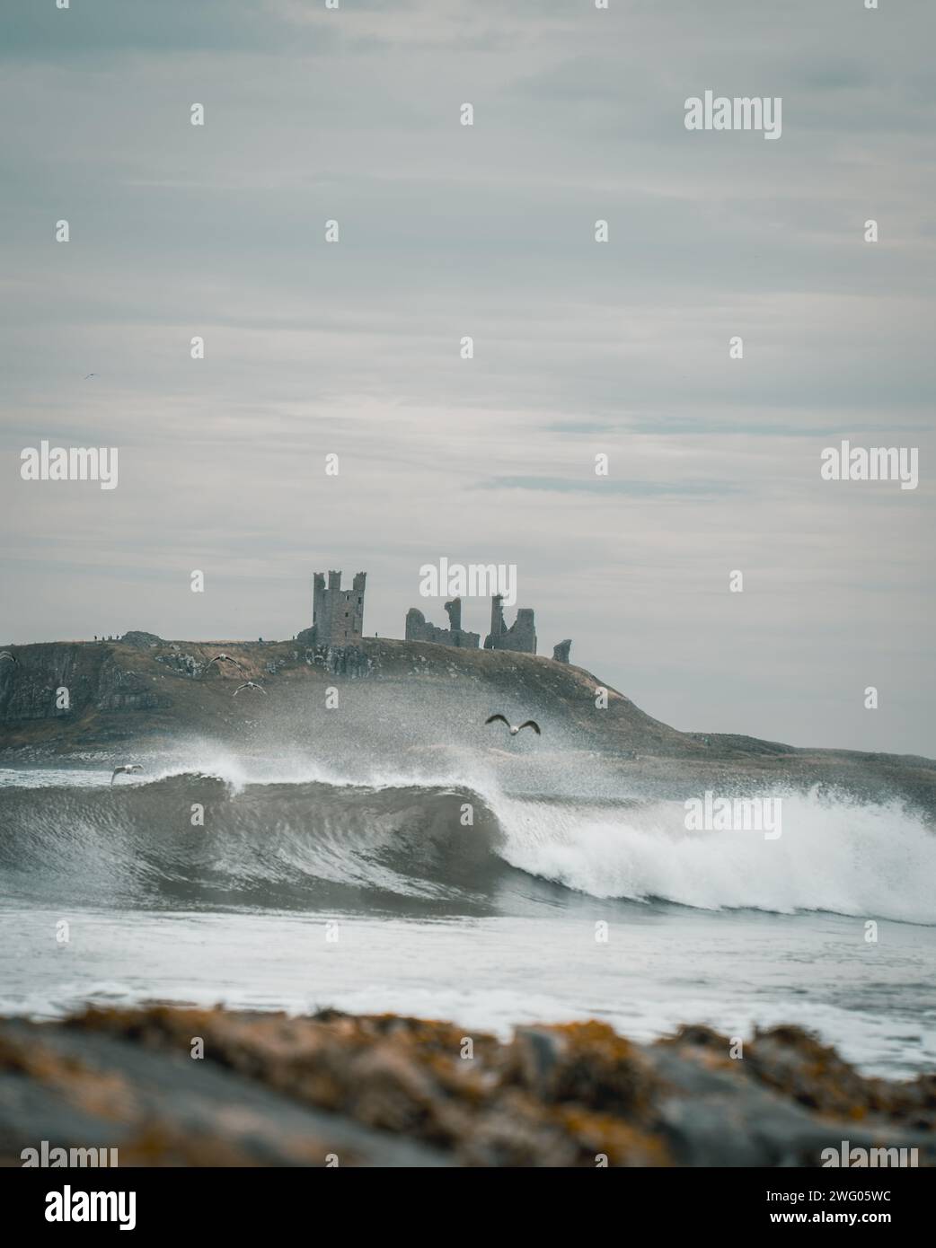 Une vue panoramique des vagues de la mer rugueuse avec les ruines du château en arrière-plan Banque D'Images Une vue panoramique des vagues de la mer rugueuse avec les ruines du château en arrière-plan Banque D'Images