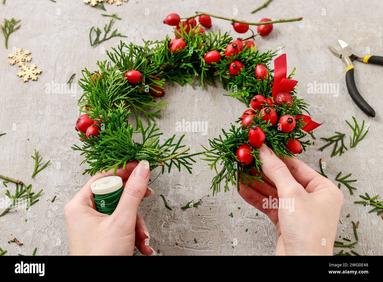 Un fleuriste au travail : Comment faire de noël traditionnelle couronne de porte avec thuja brindilles et Wild Rose fruits. Pas à pas, tutoriel. Banque D'Images