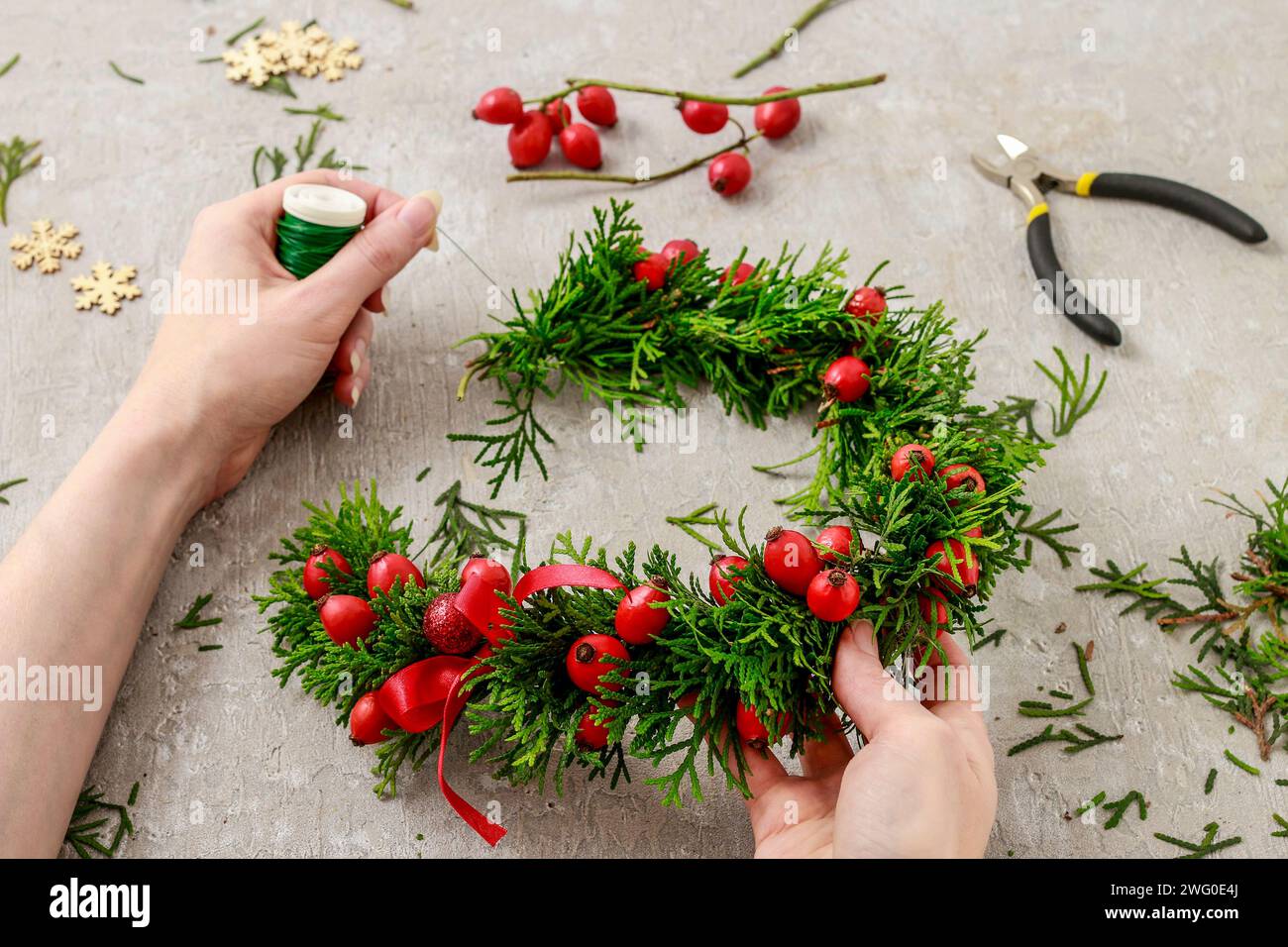 Un fleuriste au travail : Comment faire de noël traditionnelle couronne de porte avec thuja brindilles et Wild Rose fruits. Pas à pas, tutoriel. Banque D'Images