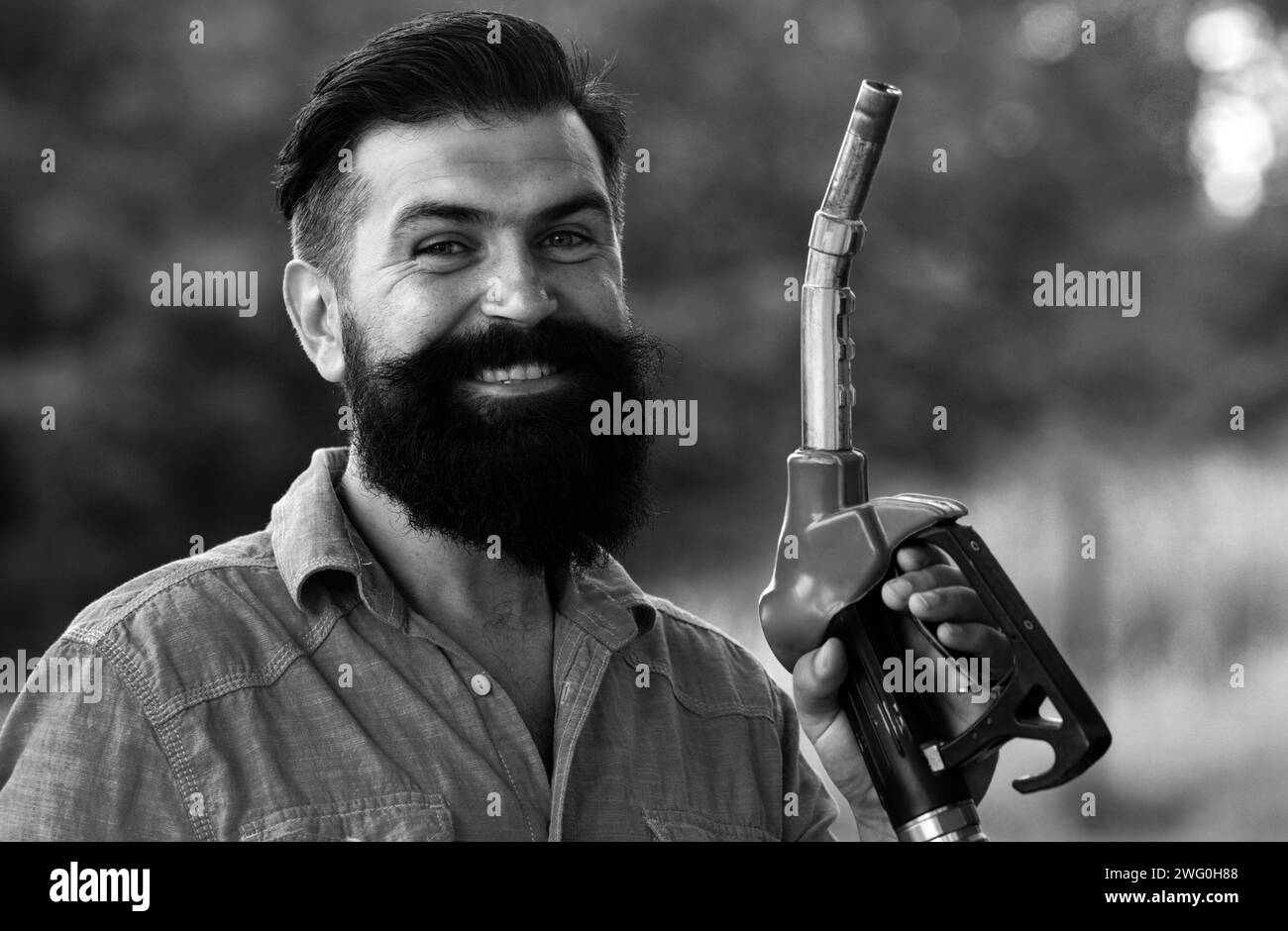 Portrait d'un homme souriant faisant le plein d'essence à la station-service. Homme sur les buses de remplissage de la pompe à essence. Station-service. Portrait de l'homme barbu tenir en nourrissant des nozz Banque D'Images