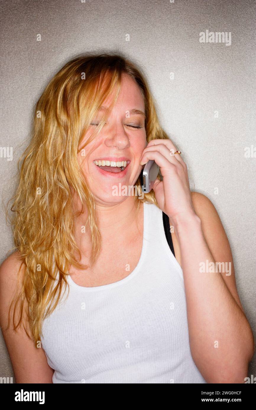Jeune femme de hanche avec de longs cheveux blonds sur le téléphone portable riant. Banque D'Images