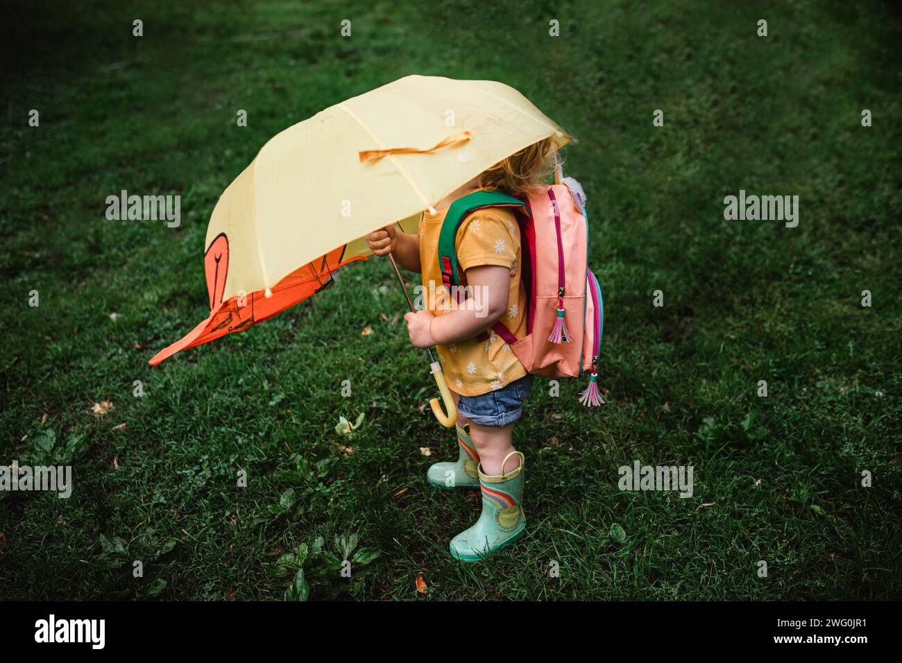 Enfant en bas âge portant un sac à dos et des bottes de pluie sous un parapluie Banque D'Images