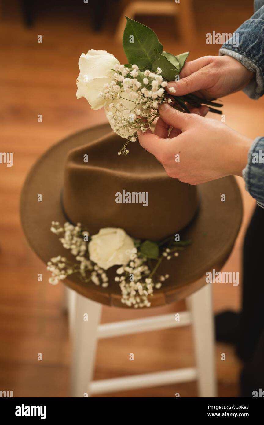 Angle élevé des mains de la personne tenant des fleurs à mettre sur un chapeau brun Banque D'Images