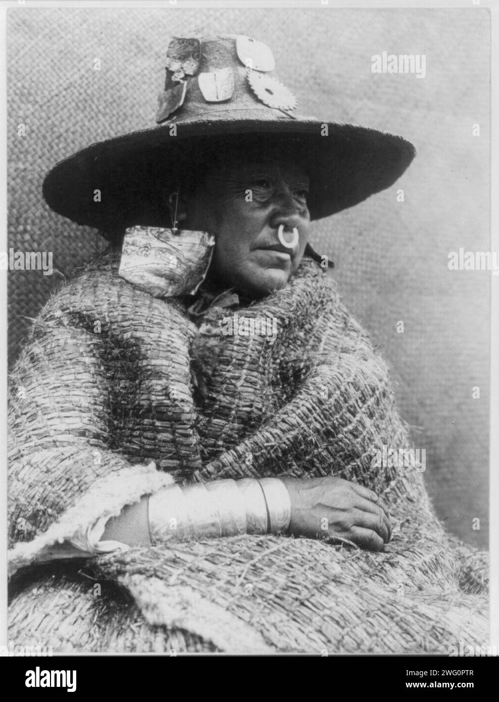 La fille d'un chef, Nakoaktok, c1914. Nakoaktok femme, portrait en demi-longueur, face à droite, assise, portant une couverture, un chapeau avec des ornements de coquille, de grandes boucles d'oreilles, une bague de nez, et plusieurs bracelets. Banque D'Images