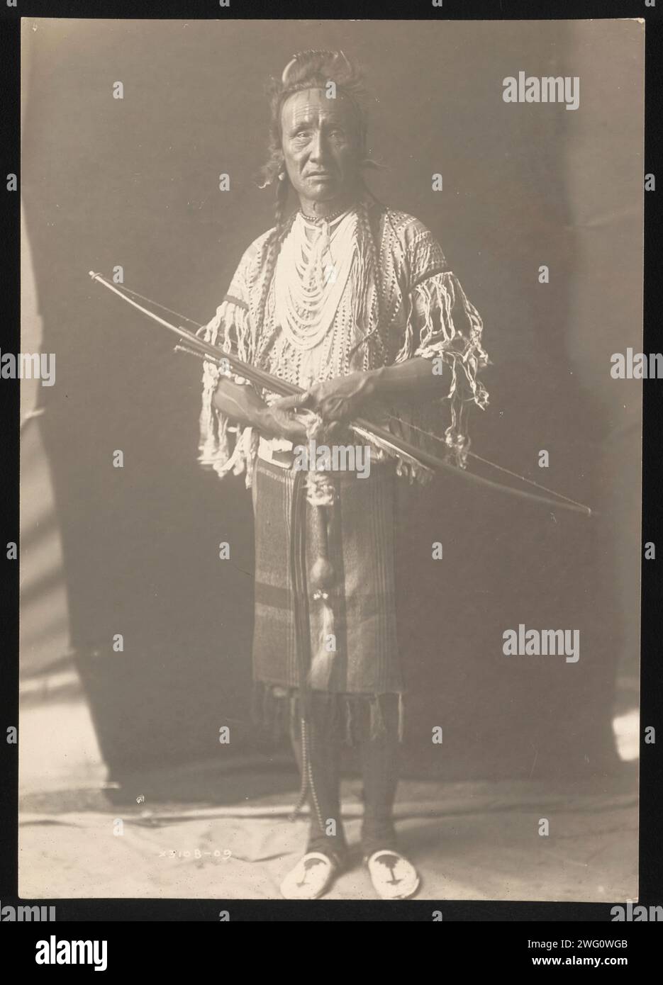 Crow Chief, 1910. La photographie montre le portrait en pied de l'ours grizzli, avec les cheveux tressés, portant des vêtements traidtional et plusieurs colliers, debout, tenant l'arc, face à l'avant. Banque D'Images Crow Chief, 1910. La photographie montre le portrait en pied de l'ours grizzli, avec les cheveux tressés, portant des vêtements traidtional et plusieurs colliers, debout, tenant l'arc, face à l'avant. Banque D'Images